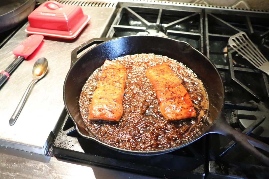 Salmon filets being basted in a glazed honey and orange sauce while pan-frying 