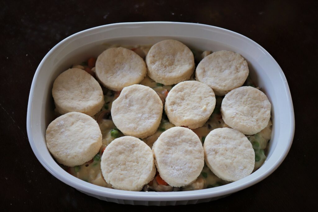 With Chicken Pot Pie With A Twist Ready For the Oven With Homemade Biscuits Over Chicken Pot Pie Filling In Pan