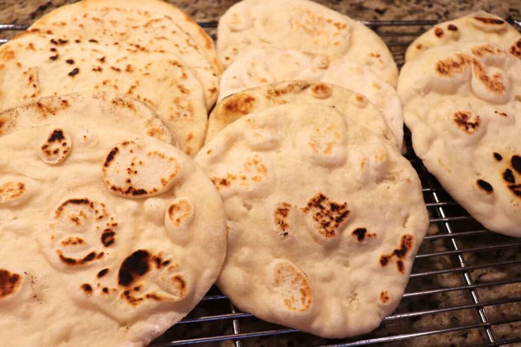 Golden pillows of freshly baked homemade naan, lovingly crafted and patiently waiting on a cooling rack to grace your table with their warm, pillowy goodness. The aroma alone is enough to transport you to a world of delightful flavors.